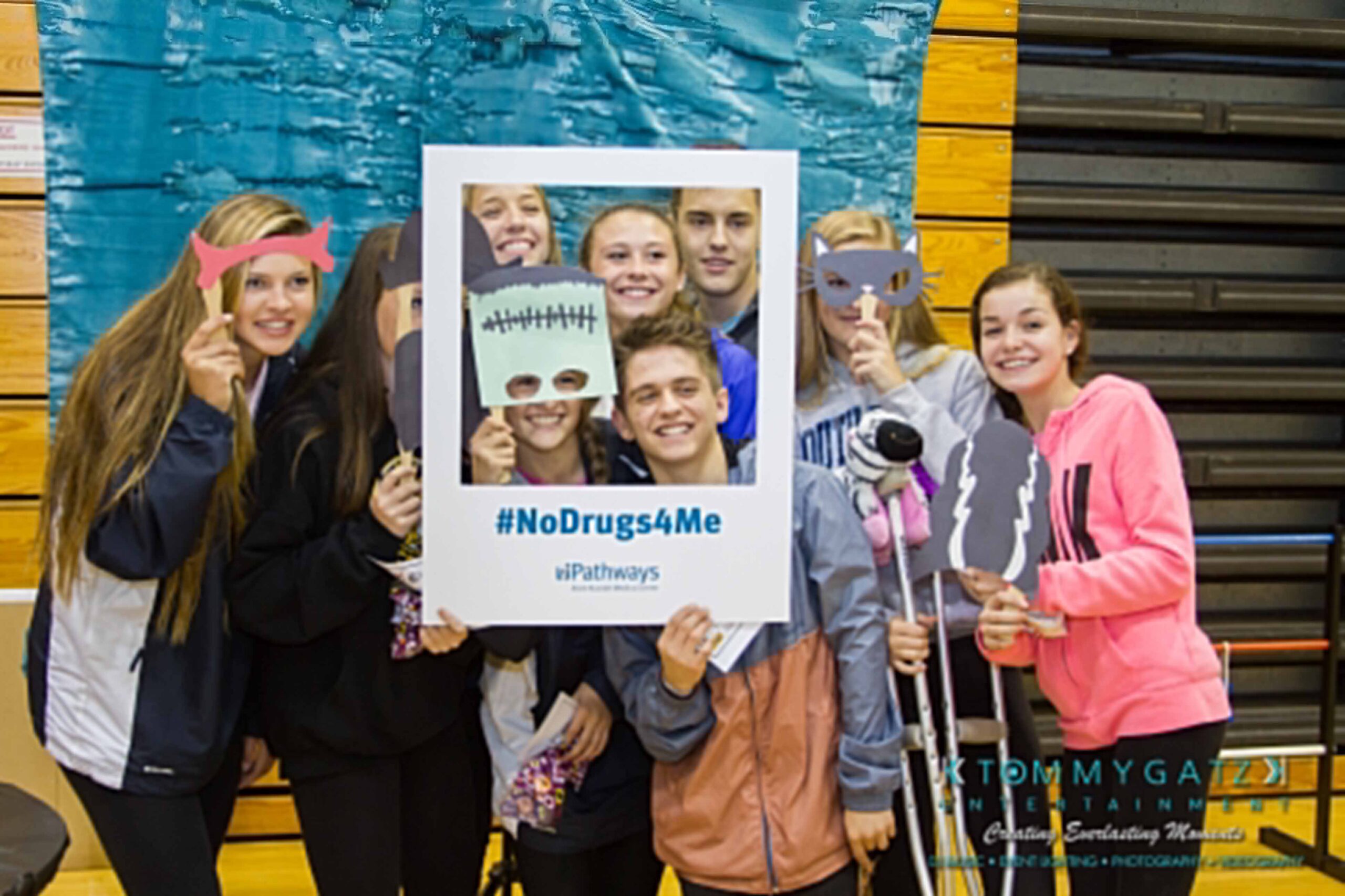 Ford-Driving-Skills-For-Life-9 - TOMMY GATZ ENTERTAINMENT Group of smiling people posing with props and a frame that reads "#NoDrugs4Me" indoors against a blue and wood background.