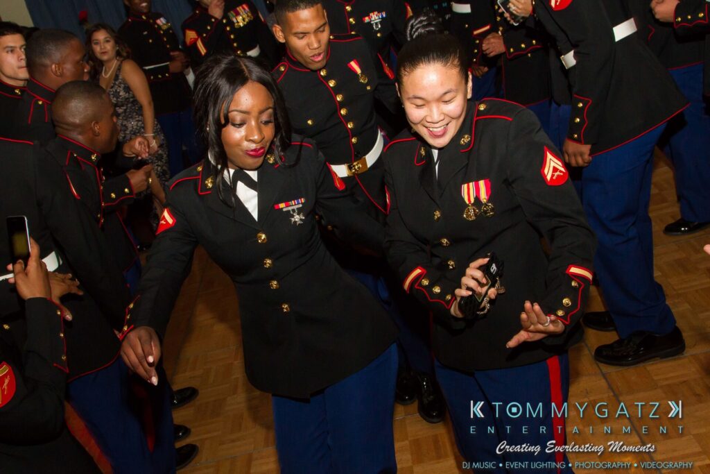 Marine-Lo-Res-156 - TOMMY GATZ ENTERTAINMENT Two Marines in dress uniforms dance at a formal event with people in similar attire in the background.