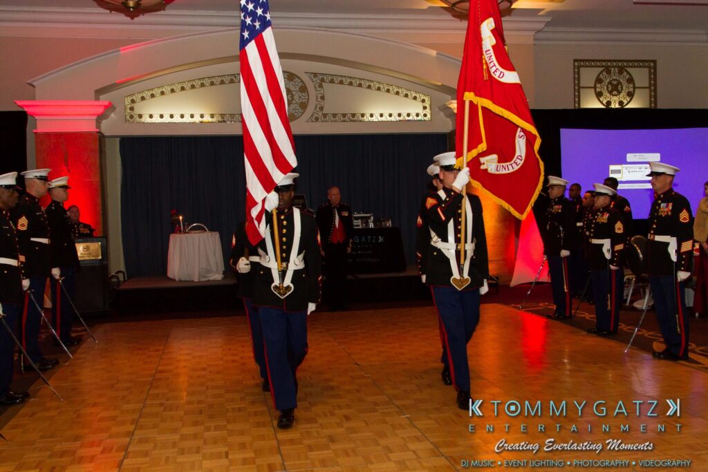 Marine-Lo-Res-28 - TOMMY GATZ ENTERTAINMENT Color guard members in ceremonial uniform present the American and Marine Corps flags on a dance floor, surrounded by uniformed personnel.