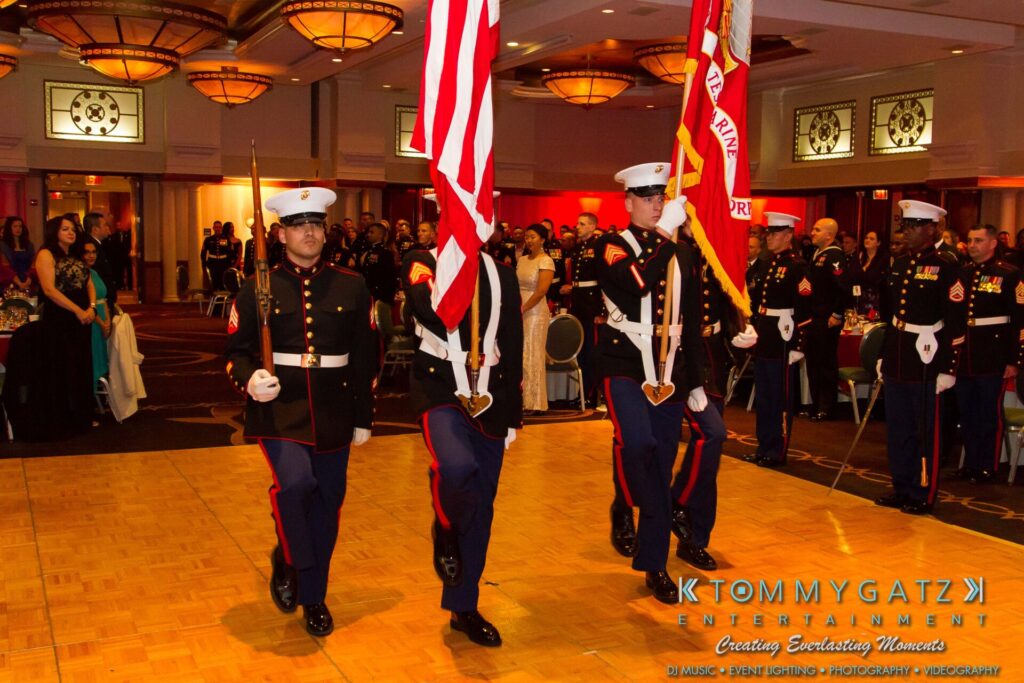 Marine-Lo-Res-47 - TOMMY GATZ ENTERTAINMENT U.S. Marines in dress uniforms perform a color guard ceremony at an indoor event with attendees watching.