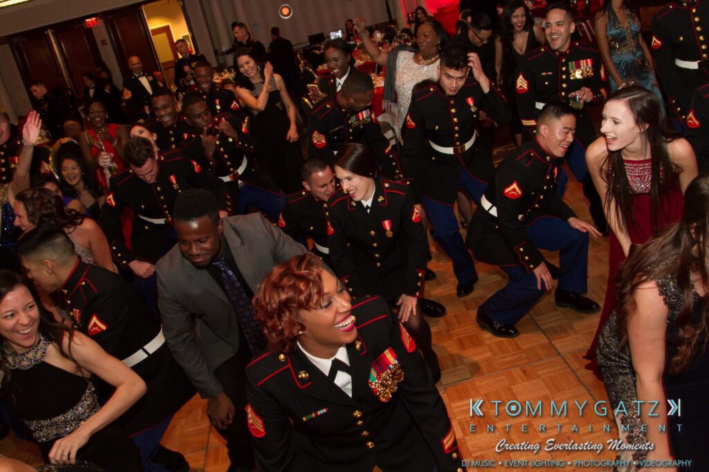 Marine-Lo-Res-91 - TOMMY GATZ ENTERTAINMENT A group of people, including uniformed military personnel, dance and celebrate at an indoor event.
