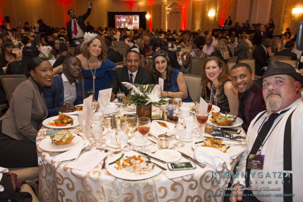 Pillar-Awards-Final-3-24-17-Blog-WM-116 - TOMMY GATZ ENTERTAINMENT A group of people sits around a decorated table at a formal event, with plates of food and drinks, in a large banquet hall.