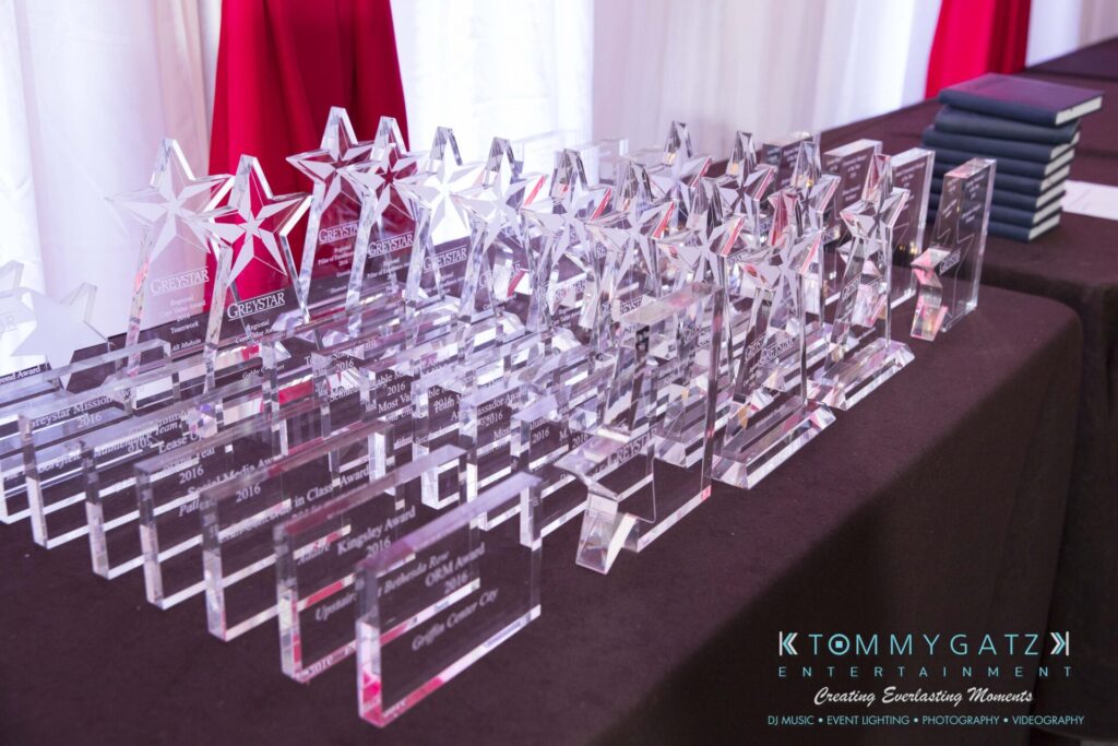 A table with multiple transparent star-shaped awards and plaques displayed in rows, with a logo and promotional text printed on the tablecloth.