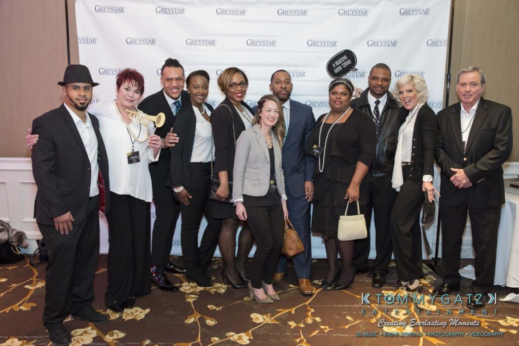 Pillar-Awards-Final-3-24-17-Blog-WM-33 - TOMMY GATZ ENTERTAINMENT A group of people posing together in front of a branded backdrop at an event. Some are holding props, including a trophy and a sign. They are dressed in business and casual attire.