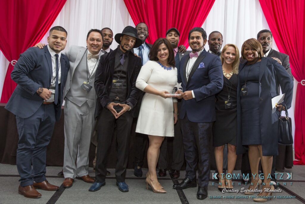 Pillar-Awards-Final-3-24-17-Blog-WM-396 - TOMMY GATZ ENTERTAINMENT A group of people in formal attire stand together on a stage with red and white drapes in the background, holding awards.