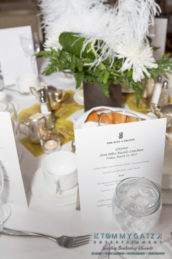 Pillar-Awards-Final-3-24-17-Blog-WM-7 - TOMMY GATZ ENTERTAINMENT Elegant table setting with a formal menu and decorations at The Ritz-Carlton. Glass of water, silverware, and white feather centerpiece on display.
