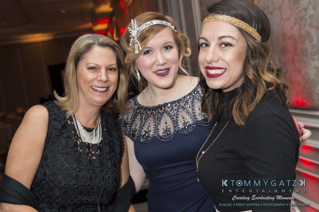 Pillar-Awards-Final-3-24-17-Blog-WM-70 - TOMMY GATZ ENTERTAINMENT Three people smiling at a formal event, with two wearing headbands and evening dresses. A logo in the corner reads "Tommy Gatz Entertainment.