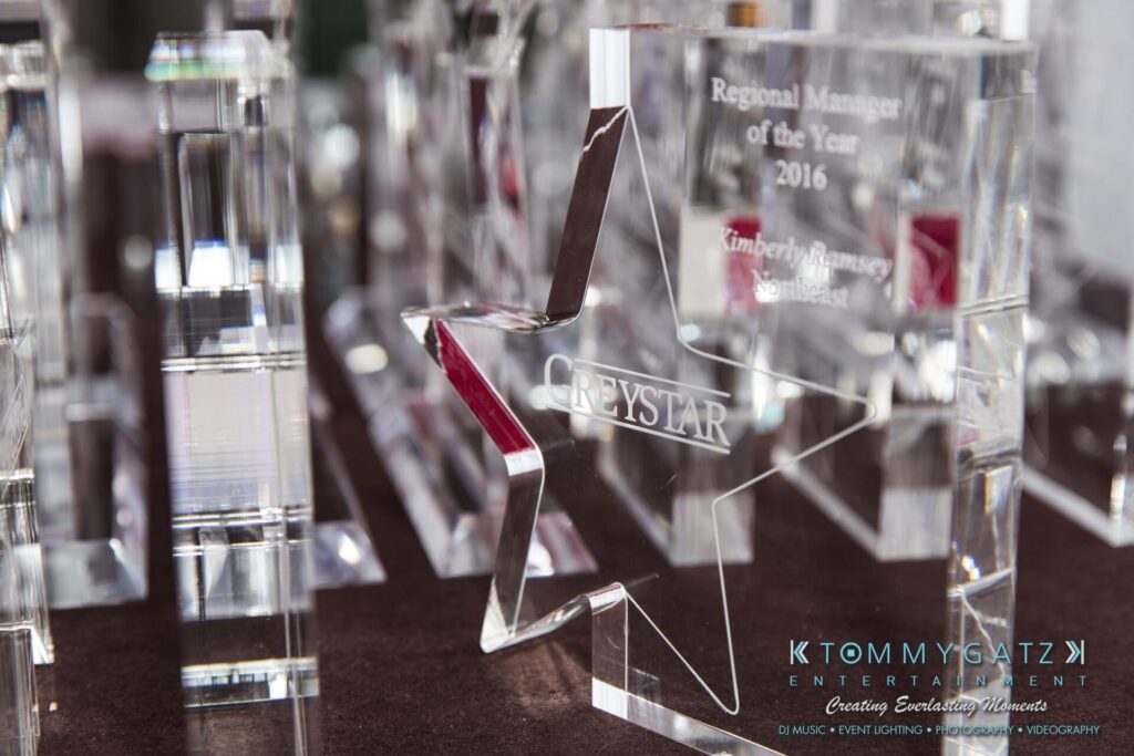 Pillar-Awards-Final-3-24-17-Blog-WM-78 - TOMMY GATZ ENTERTAINMENT Close-up of a star-shaped crystal award labeled "Greystar" amidst other clear awards. Logo for Tommy Gatz Entertainment visible at the bottom right.