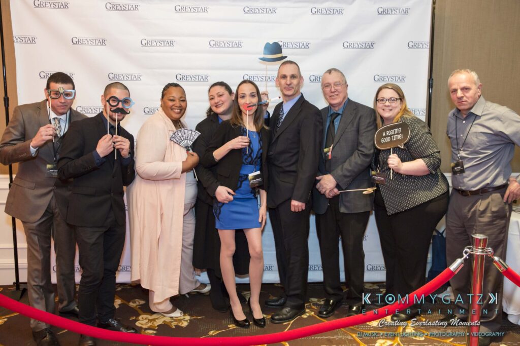Pillar-Awards-Final-3-24-17-Blog-WM-9 - TOMMY GATZ ENTERTAINMENT A group of people posing with props in front of a backdrop that reads "GREYSTAR," standing on a carpeted floor with a red velvet rope barrier.
