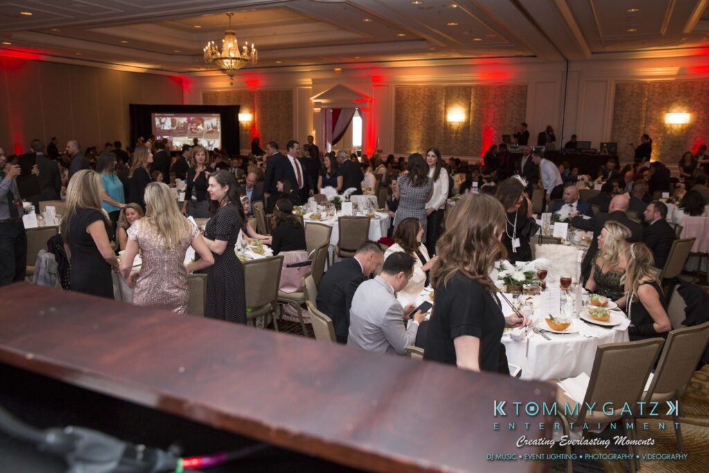 Pillar-Awards-Final-3-24-17-Blog-WM-97 - TOMMY GATZ ENTERTAINMENT A formal banquet with many attendees seated at round tables in an elegant ballroom. A projector screen displays an image in the background.