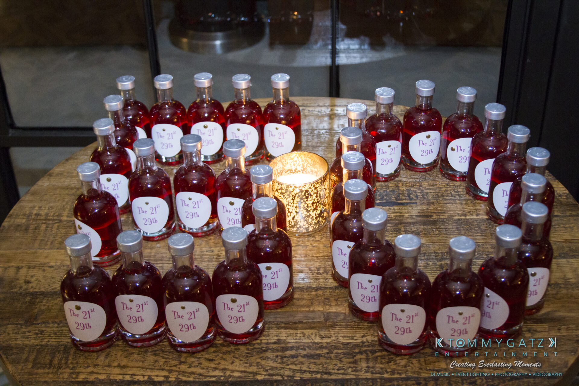 SUSAN_50TH_BIRTHDAY_WATERMARK29 1 - TOMMY GATZ ENTERTAINMENT A table with small bottles of red liquid surrounding a lit candle. The labels read "The 21st/29th.
