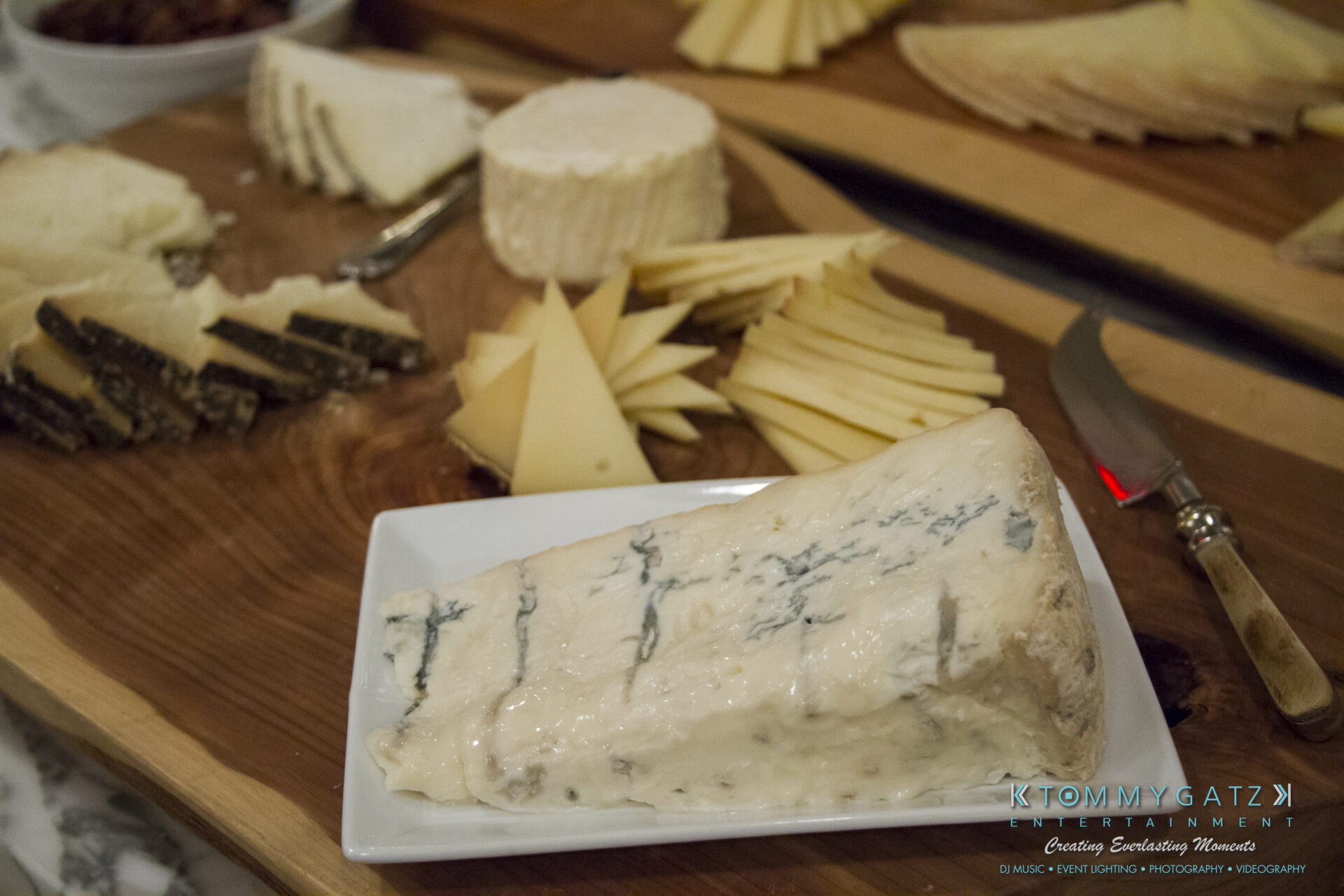 SUSAN_50TH_BIRTHDAY_WATERMARK3 - TOMMY GATZ ENTERTAINMENT A platter with various cheeses, including a prominent wedge of blue cheese in the foreground, displayed on a wooden board.