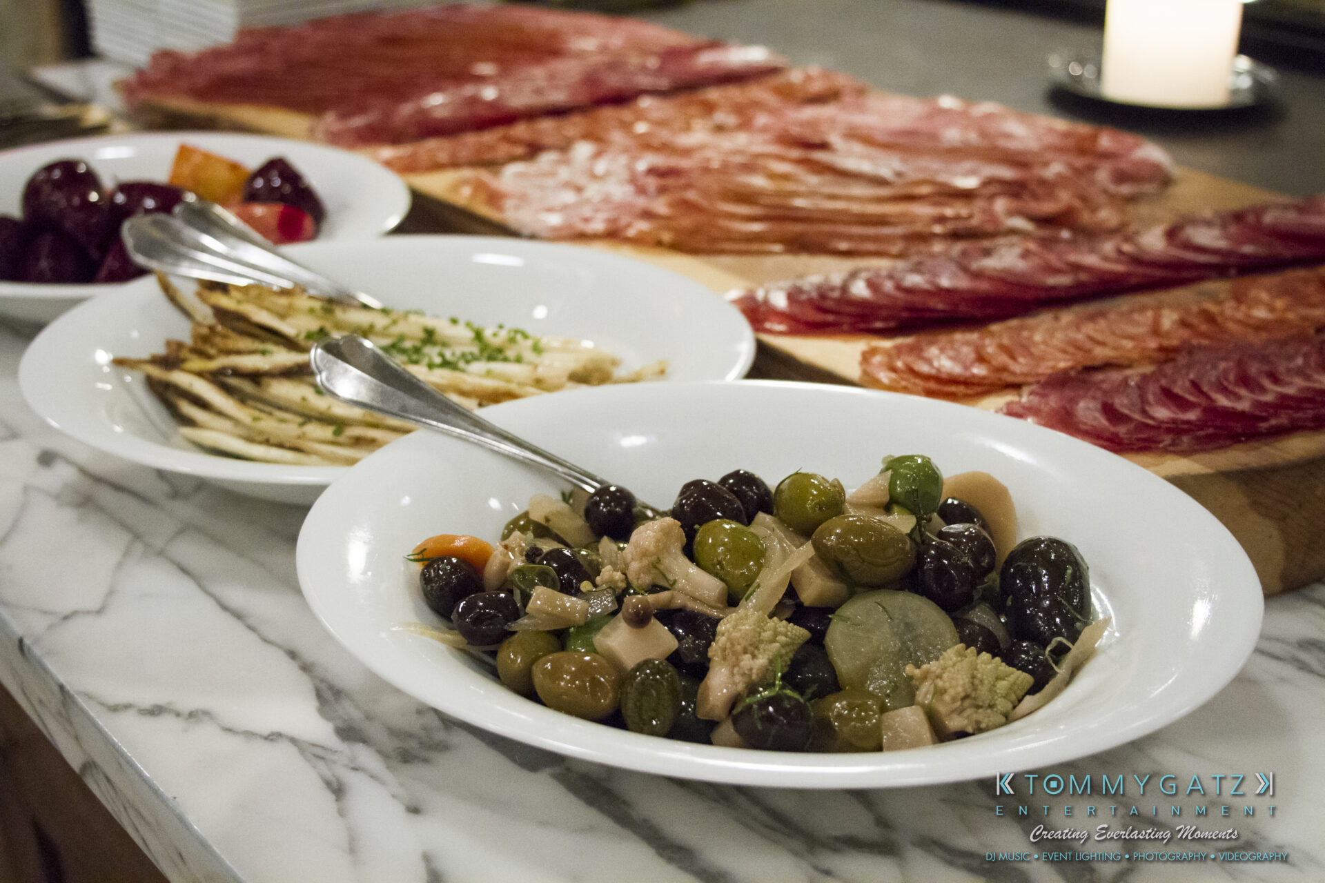 SUSAN_50TH_BIRTHDAY_WATERMARK4 - TOMMY GATZ ENTERTAINMENT An assortment of charcuterie with cured meats, olives, pickles, and sliced bread is displayed on a marble countertop.