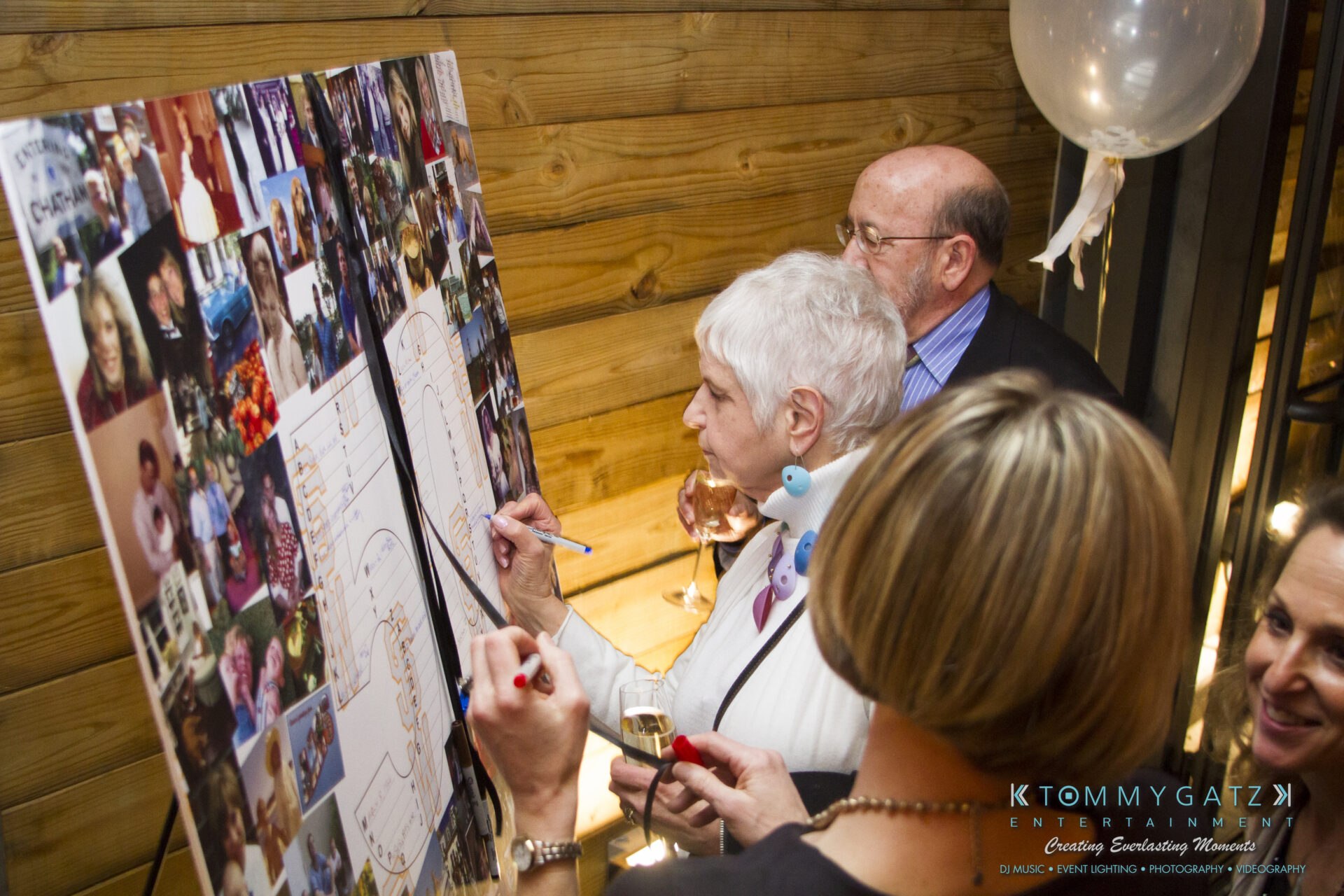 SUSAN_50TH_BIRTHDAY_WATERMARK49 - TOMMY GATZ ENTERTAINMENT People are signing a large photo collage on a wooden wall during an event.