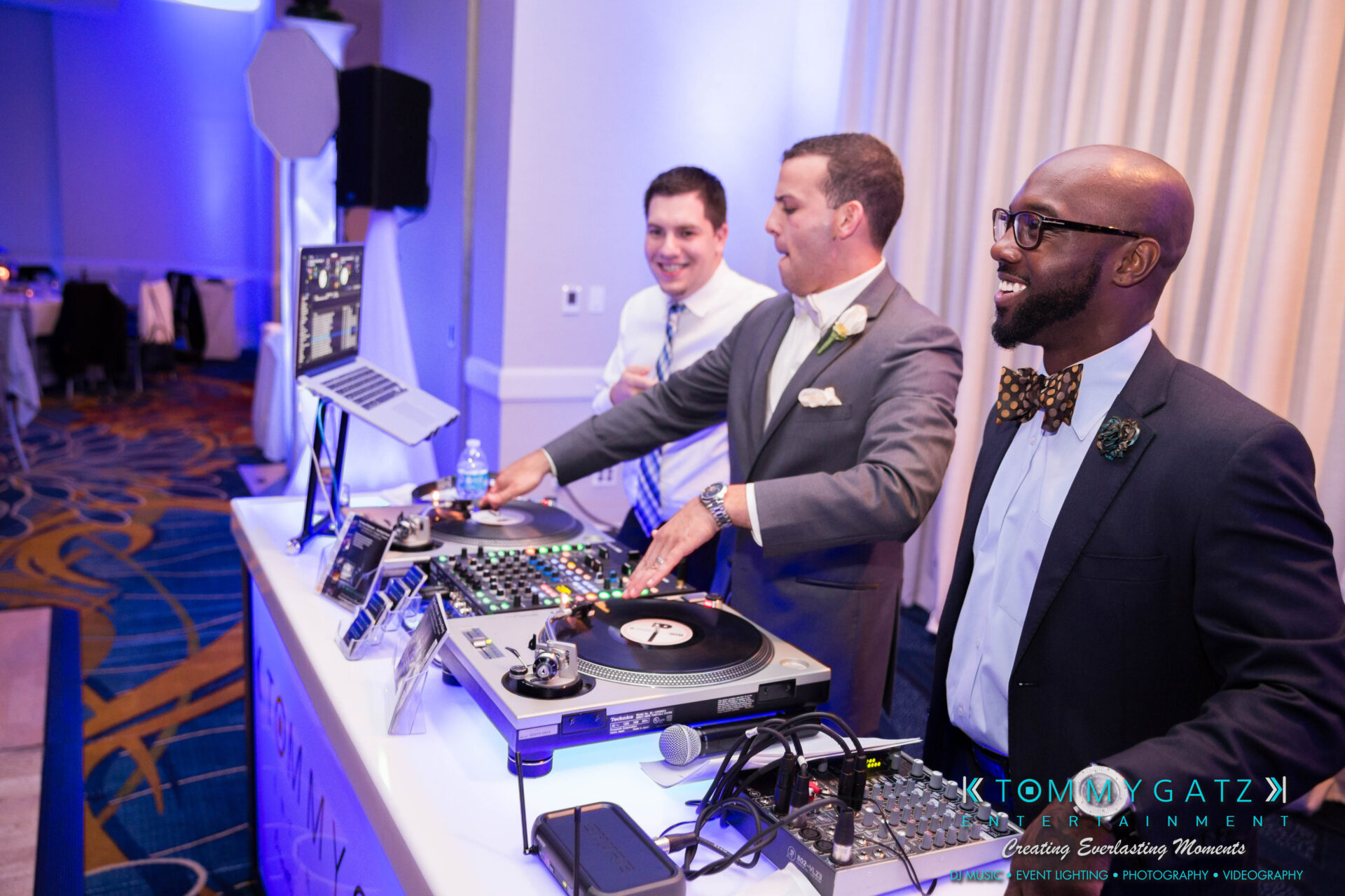 untitled-17 - TOMMY GATZ ENTERTAINMENT Three DJs in formal attire are standing behind a DJ booth with turntables and a laptop at an event.