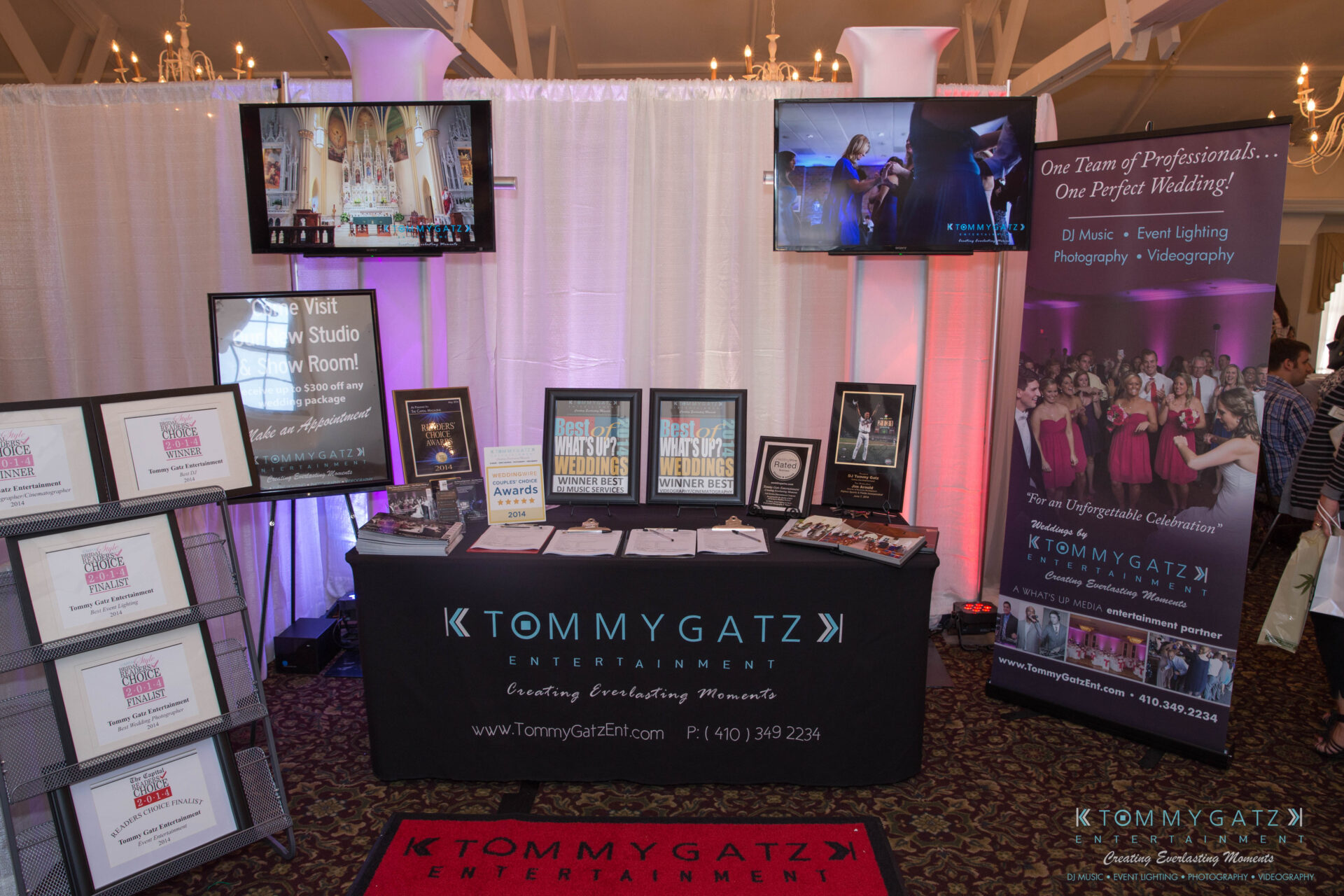 untitled-23 - TOMMY GATZ ENTERTAINMENT A booth display featuring Tommy Gatz Entertainment with awards, promotional materials, and screens showcasing event services for weddings and special occasions.