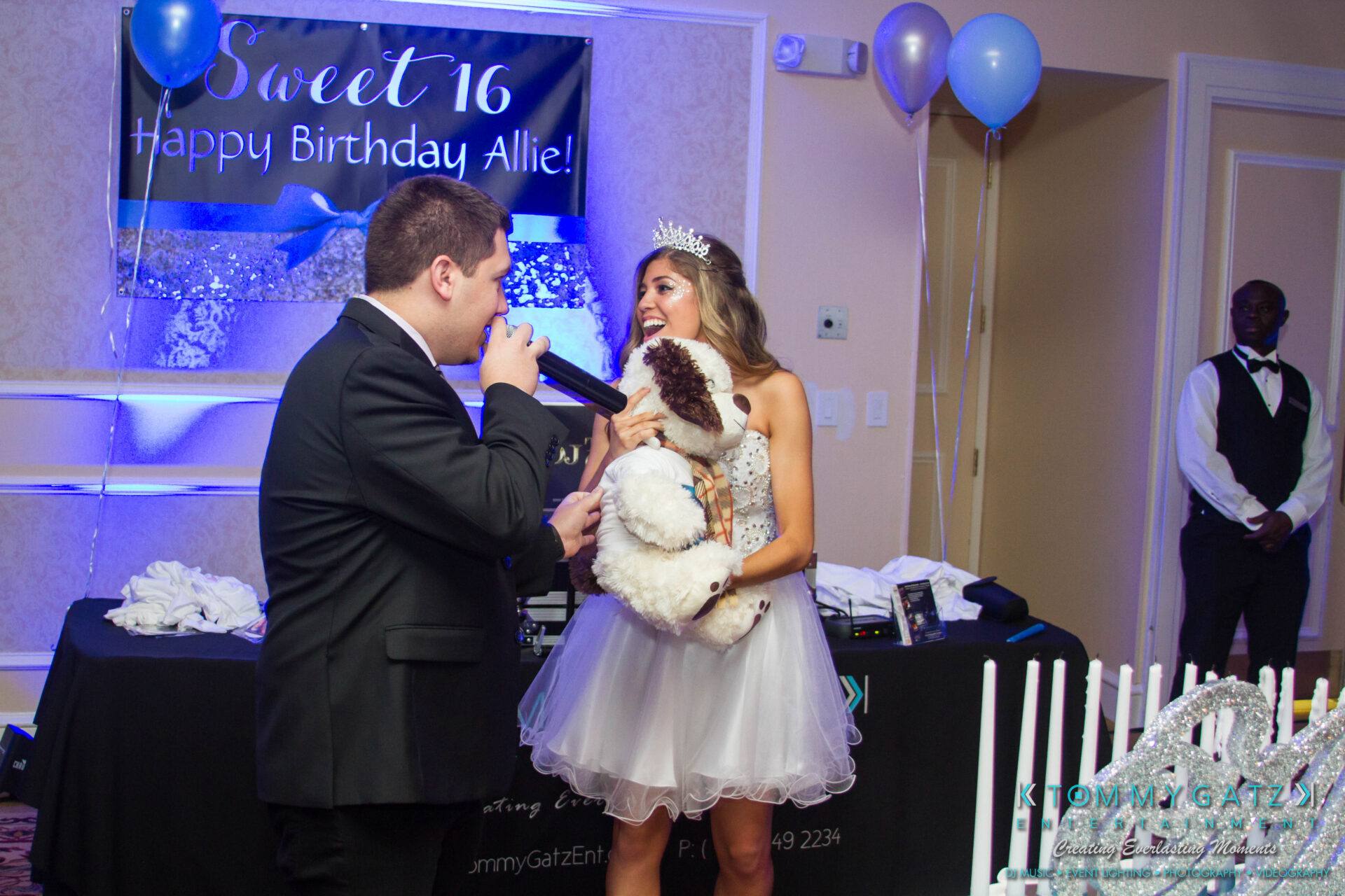 untitled-32 - TOMMY GATZ ENTERTAINMENT A girl in a white dress holds a stuffed animal and smiles while a person in a suit speaks into a microphone. A "Sweet 16" birthday banner and balloons are in the background.