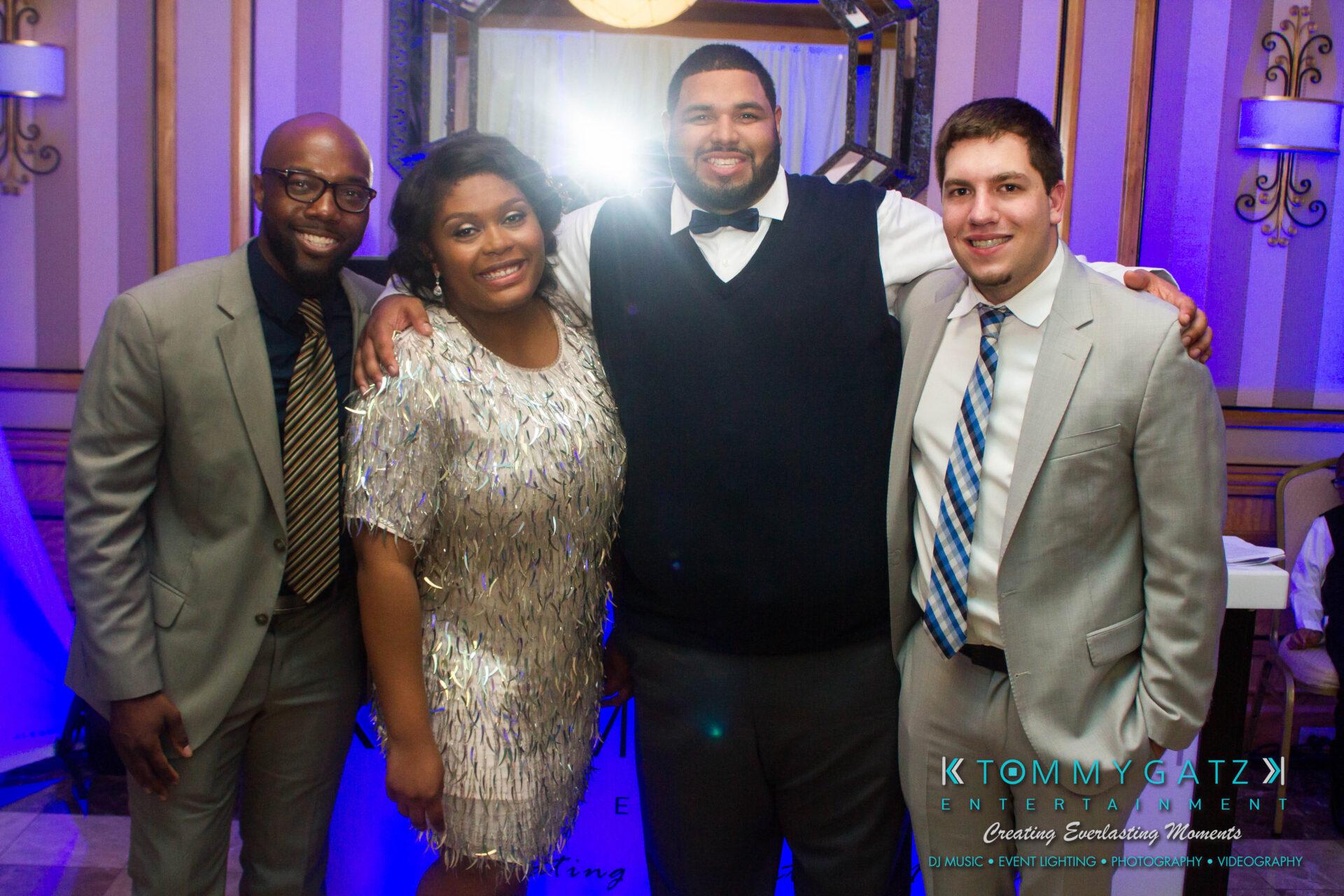 untitled-35 - TOMMY GATZ ENTERTAINMENT Four people smiling and standing together in a formal setting, with a logo at the bottom right corner.