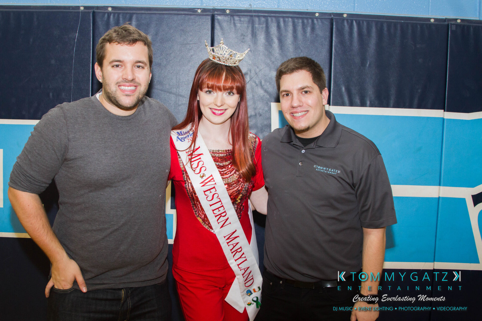 untitled-36 - TOMMY GATZ ENTERTAINMENT Three people posing together; a woman in a red outfit and crown with a "Miss Western Maryland" sash stands between two men wearing casual shirts.
