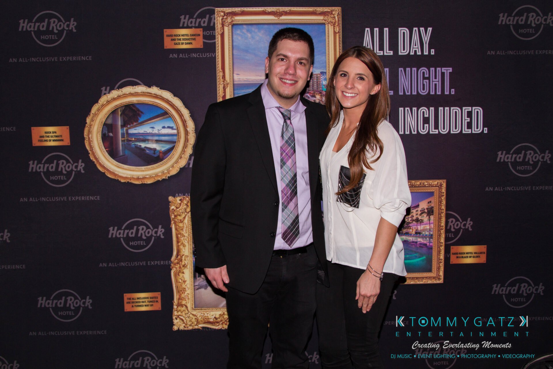 untitled-8 - TOMMY GATZ ENTERTAINMENT A man and a woman pose together in front of a backdrop with Hard Rock branding and framed paintings.
