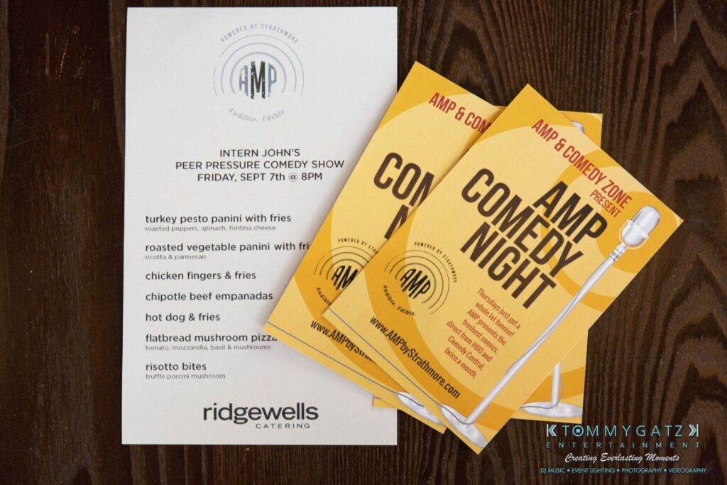 18A0029 - TOMMY GATZ ENTERTAINMENT Menu and flyers for AMP Comedy Night event featuring food options like turkey pesto panini and chipotle beef empanadas, with Ridgewells Catering and event details.