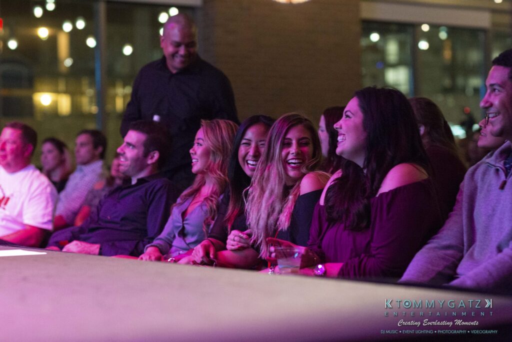 18A0098A-1 - TOMMY GATZ ENTERTAINMENT A group of people sitting together, smiling and laughing, at an indoor event.