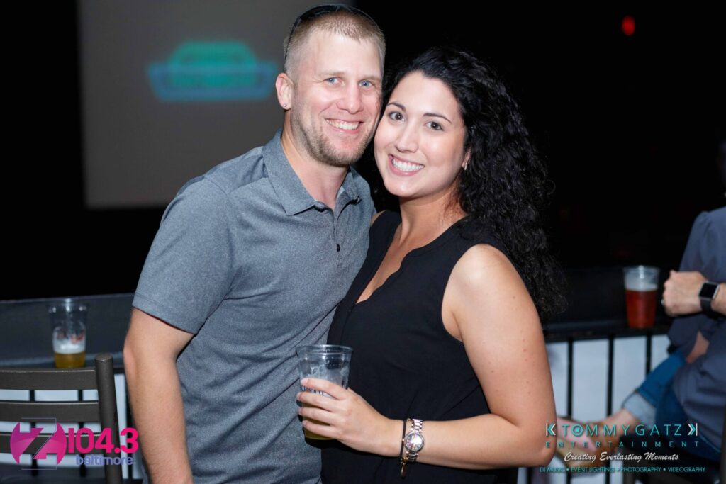 Intern-John-Peer-Pressure-Comedy-Show-Baltimore-7-14-17-Blog-Watermark-13 - TOMMY GATZ ENTERTAINMENT A smiling man and woman stand close together, holding drinks, at an event. Logos for "Z 104.3 Baltimore" and "Tommy Gatz Entertainment" are in the lower corners.