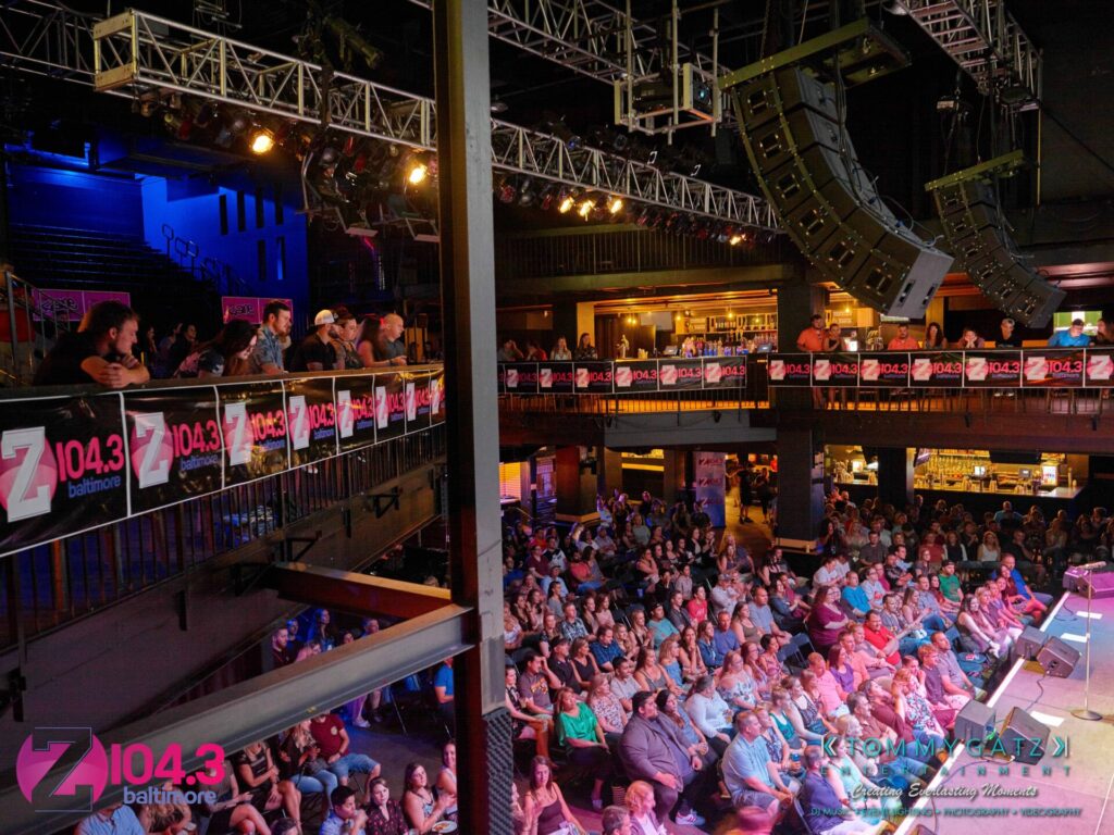 Intern-John-Peer-Pressure-Comedy-Show-Baltimore-7-14-17-Blog-Watermark-17 - TOMMY GATZ ENTERTAINMENT An indoor concert venue with a crowded audience seated in front of a stage. Banners for "Z104.3 Baltimore" are displayed throughout the venue.