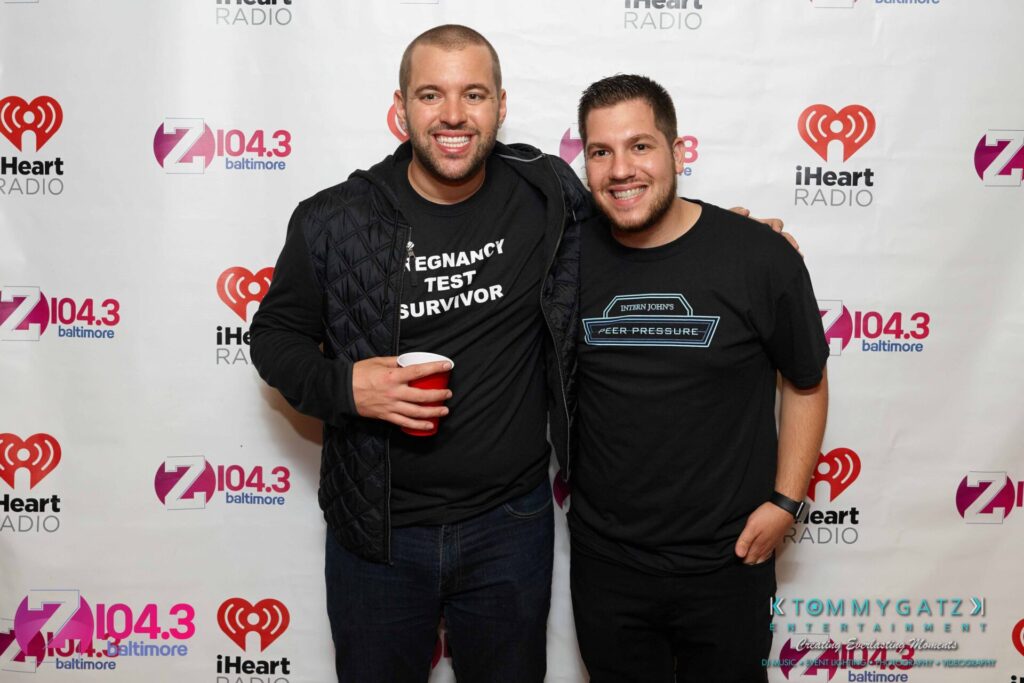Intern-John-Peer-Pressure-Comedy-Show-Baltimore-7-14-17-Blog-Watermark-45 - TOMMY GATZ ENTERTAINMENT Two men posing together at an event, standing in front of a backdrop featuring logos of Z104.3 Baltimore and iHeartRadio. One is holding a red cup.