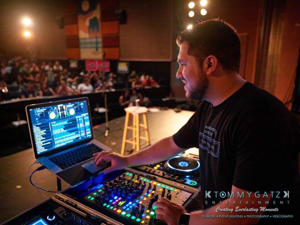 Intern-John-Peer-Pressure-Comedy-Tour-Arlington-7-21-17-low-res-Watermark-44 - TOMMY GATZ ENTERTAINMENT A DJ is performing on stage with a laptop and mixer, surrounded by audience members in a dimly lit venue.