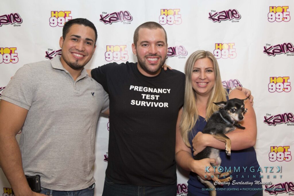 Intern-John-Pressure-Comedy-Tour-ARLINGTON-BLOG-WM-232-of-323 - TOMMY GATZ ENTERTAINMENT Three people standing together smiling in front of a backdrop with logos, one person is holding a small dog.
