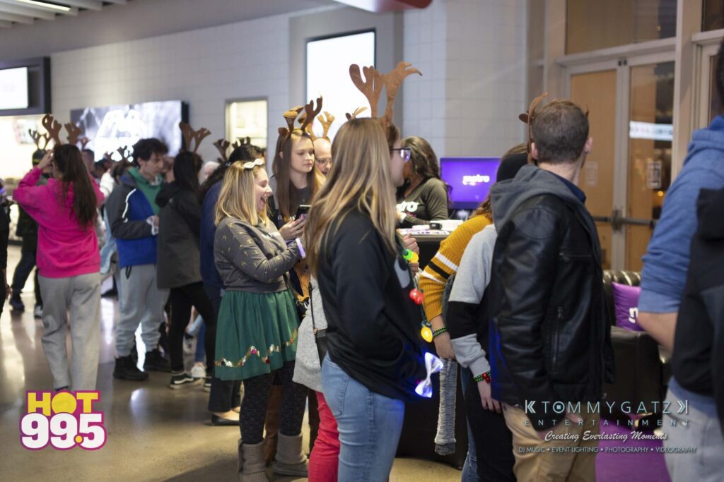 Jingle-Ball-2018-BTS-10 - TOMMY GATZ ENTERTAINMENT People wearing reindeer antlers stand in line at an event. A "Hot 99.5" logo is visible on a banner.