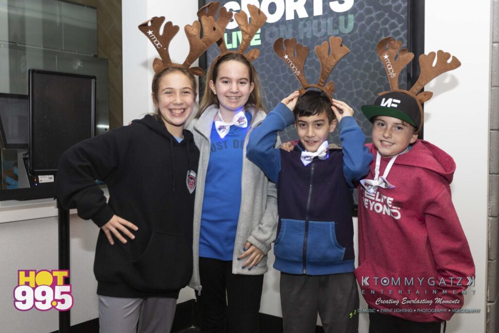 Jingle-Ball-2018-BTS-22 - TOMMY GATZ ENTERTAINMENT Four kids wearing moose antler headbands pose together, smiling. Three are in dark hoodies and one in a red hoodie. A "HOT 99.5" logo is visible in the bottom left corner.