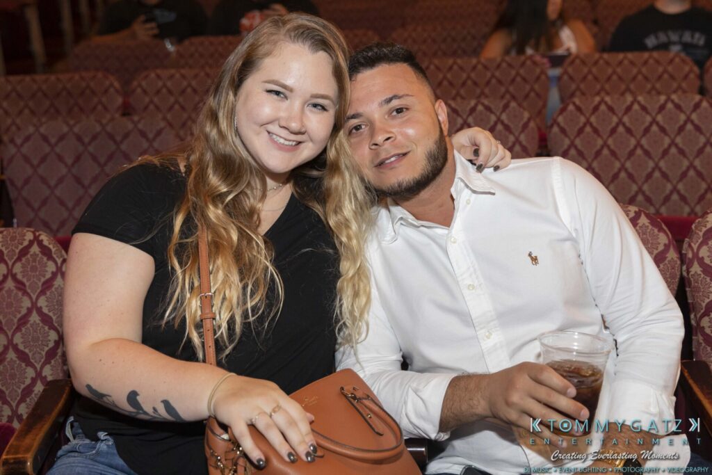 A woman and a man sitting together in theater seats. The man is holding a drink.