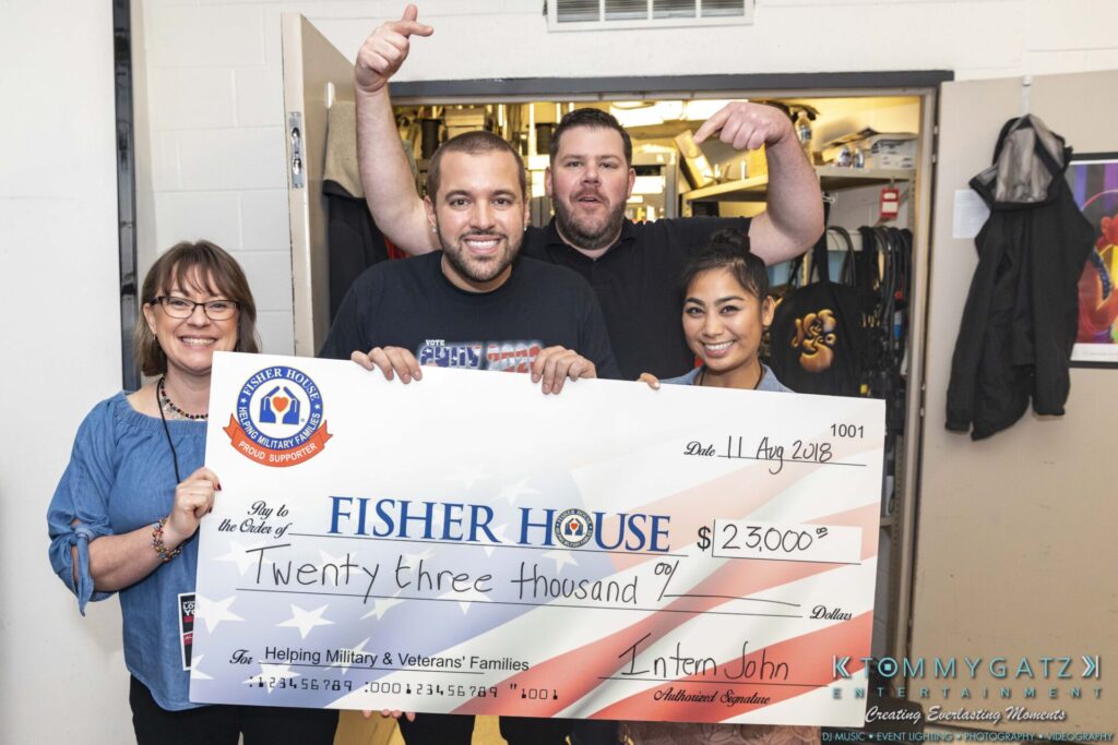 Four people holding a large check for $23,000 from Fisher House, dated August 11, 2018, supporting military and veterans' families.