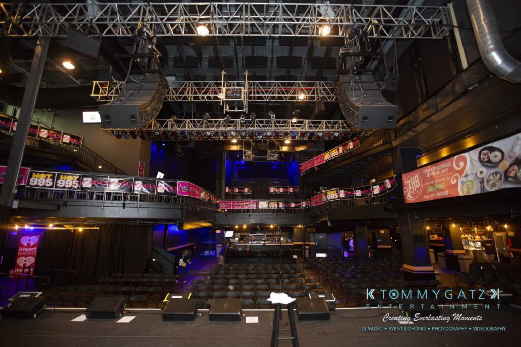 LWYD-Comedy-Tour-Baltimore-060118-FINALS-Low-Res-Watermark-1 - TOMMY GATZ ENTERTAINMENT Interior view of an empty concert venue with stage, seating, and banners. Stage lights and sound equipment are visible overhead.