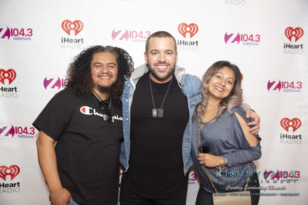 LWYD-Comedy-Tour-Baltimore-060118-FINALS-Low-Res-Watermark-300 - TOMMY GATZ ENTERTAINMENT Three people smiling in front of a backdrop with iHeart Radio and Z104.3 logos.