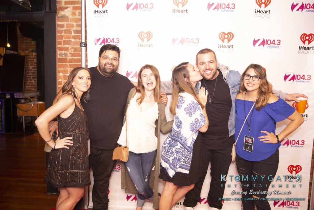 LWYD-Comedy-Tour-Baltimore-060118-FINALS-Low-Res-Watermark-313 - TOMMY GATZ ENTERTAINMENT A group of six people posing in front of a backdrop featuring iHeart Radio and Z104.3 logos at an event.