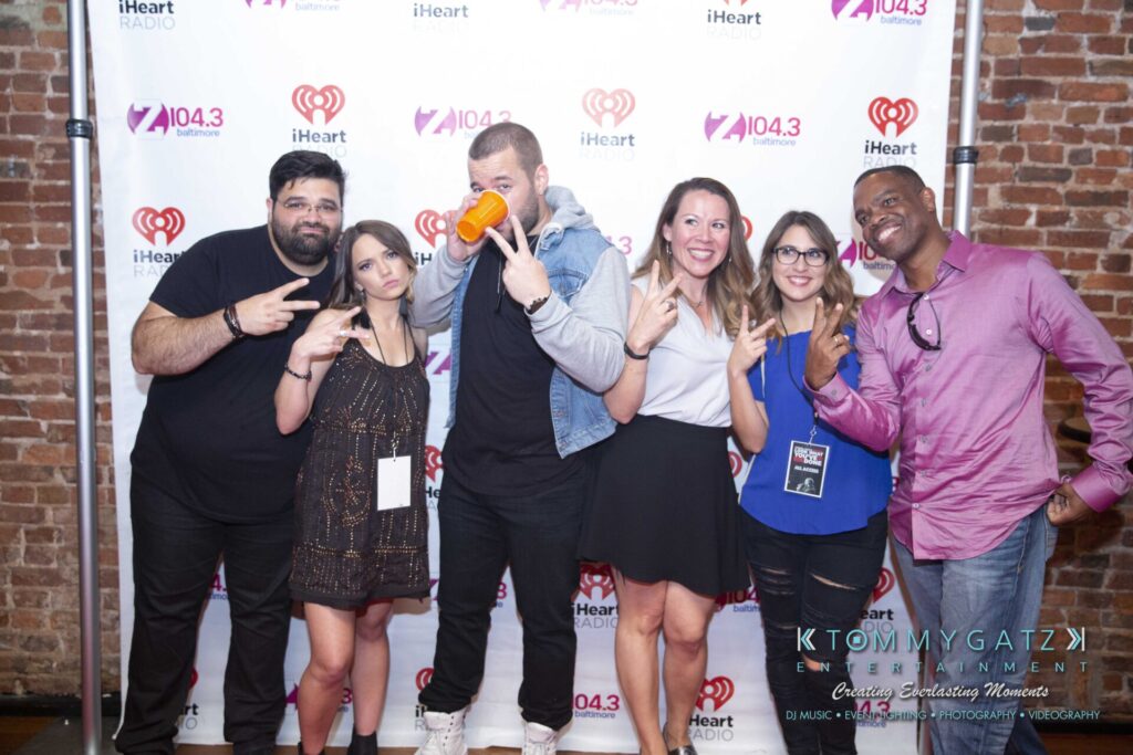 LWYD-Comedy-Tour-Baltimore-060118-FINALS-Low-Res-Watermark-324 - TOMMY GATZ ENTERTAINMENT A group of six people posing in front of a iHeartRadio and Z104.3 backdrop, making peace signs and smiling.