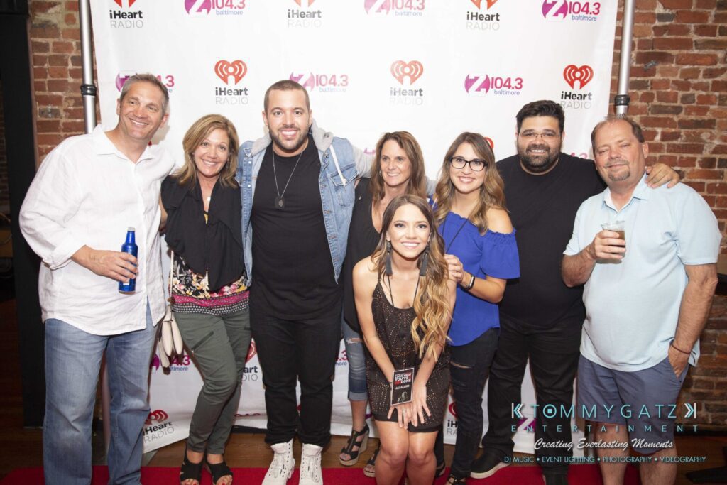 LWYD-Comedy-Tour-Baltimore-060118-FINALS-Low-Res-Watermark-403 - TOMMY GATZ ENTERTAINMENT A group of seven people posing in front of a backdrop with logos, including iHeartRadio and Z104.3.