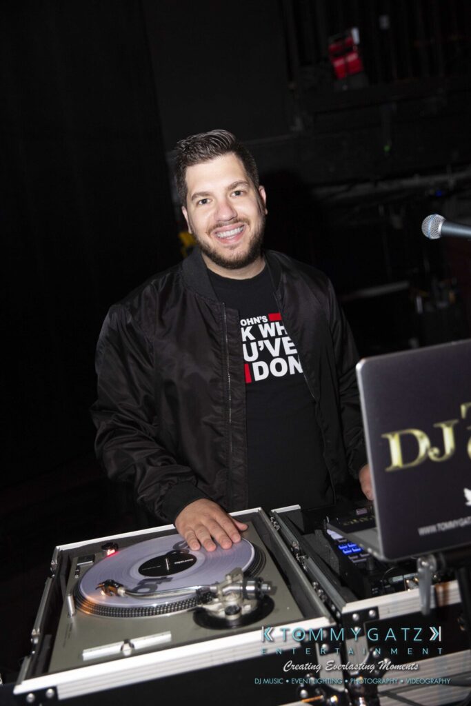 LWYD-Comedy-Tour-Baltimore-060118-FINALS-Low-Res-Watermark-421 - TOMMY GATZ ENTERTAINMENT A DJ stands behind a turntable setup, smiling.