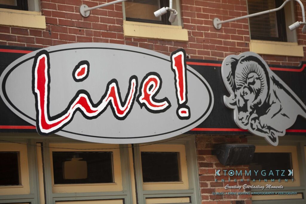 LWYD-Comedy-Tour-Baltimore-060118-FINALS-Low-Res-Watermark-8 - TOMMY GATZ ENTERTAINMENT A brick building exterior with a large "Live!" sign and a ram illustration. The logo "Tommy Gatz Entertainment" is visible at the bottom.