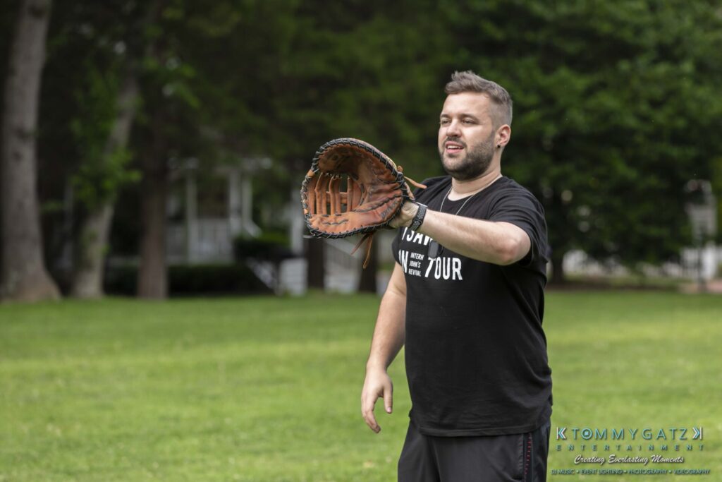 053119-Gaithersburg-ARTS-BARN-Low-Res-WM-16 - TOMMY GATZ ENTERTAINMENT A man playing catch with a baseball glove in a grassy park setting.