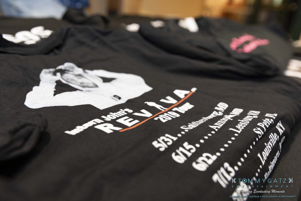 053119-Gaithersburg-ARTS-BARN-Low-Res-WM-33 - TOMMY GATZ ENTERTAINMENT A black T-shirt with "Revival 2019 Tour" details printed on it, featuring a figure in a white outfit. Tour dates and locations are listed below.
