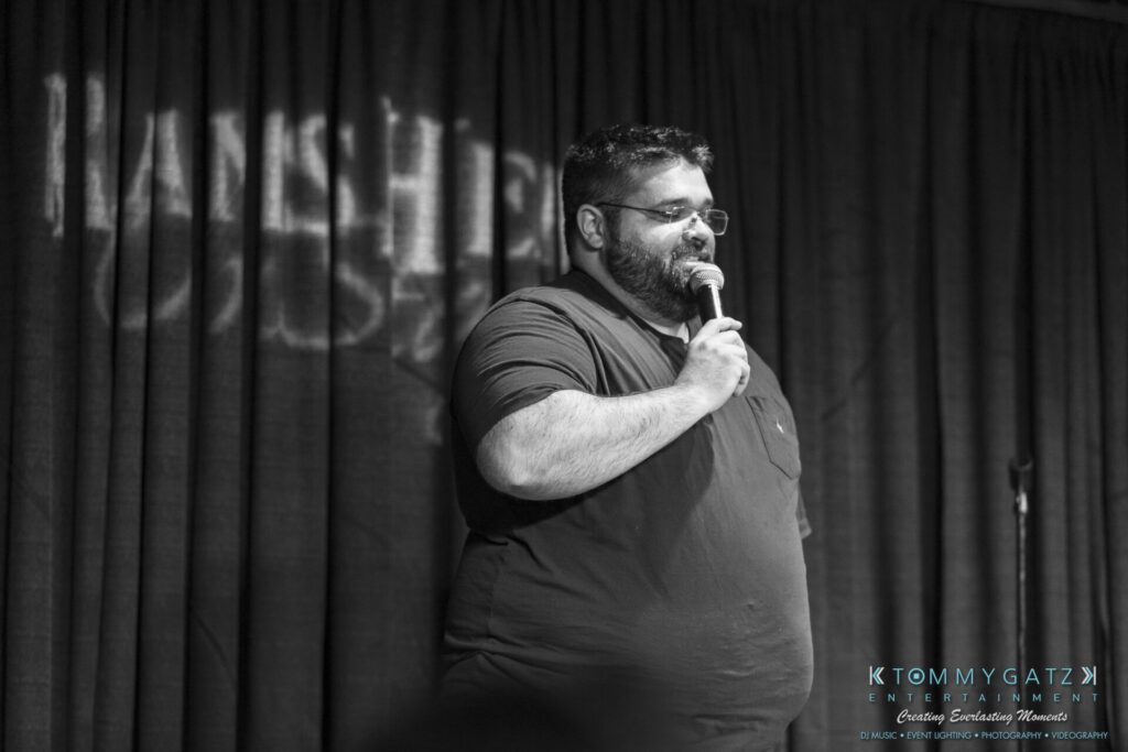 061519-Annapolis-RAMSHEAD-Low-Res-WM-89 - TOMMY GATZ ENTERTAINMENT A man standing on stage holding a microphone, with a backdrop and event branding visible.