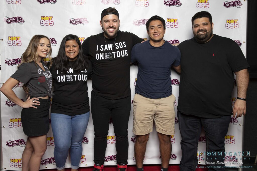 062219-Leesburg-TALLY-HO-Low-Res-WM-131 - TOMMY GATZ ENTERTAINMENT Five people standing together, smiling in front of a backdrop with "HOT 99.5" and "Kane Show" logos.