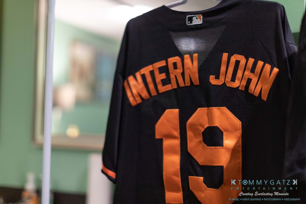 081019-Baltimore-RAMS-HEAD-Low-Res-WM-6 - TOMMY GATZ ENTERTAINMENT A black sports jersey with the name "INTERN JOHN" and the number "19" hangs indoors.