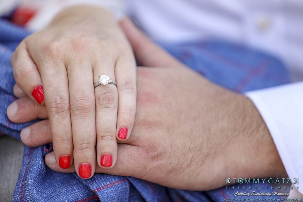 Close-up of two hands overlapping, with one wearing a diamond ring and red nail polish, resting on a blue fabric.