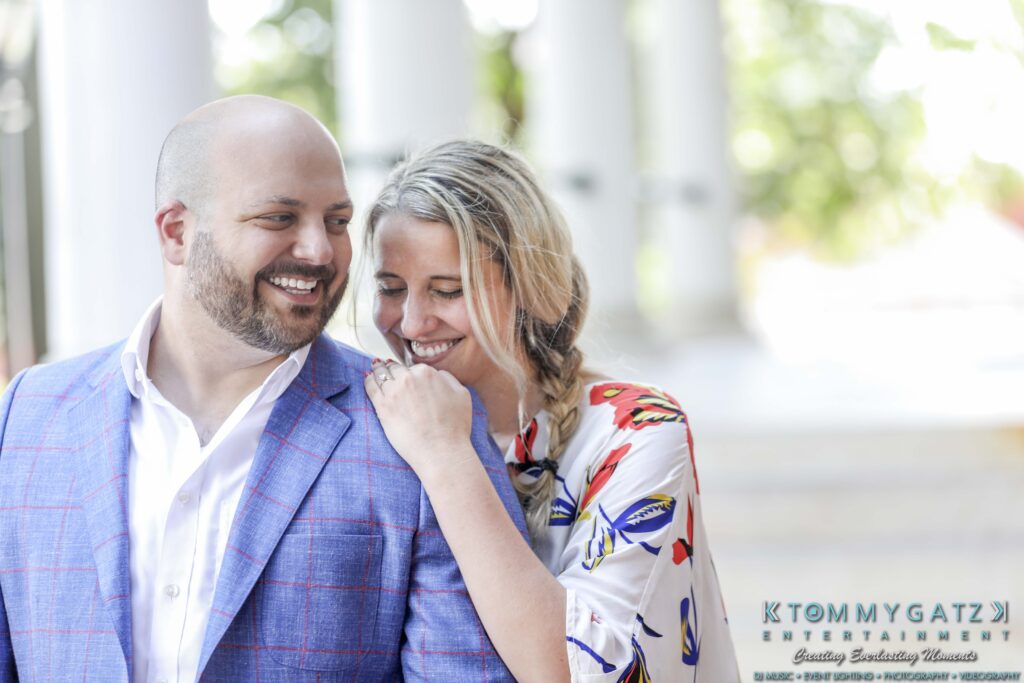 A man in a blue plaid suit and a woman in a floral outfit smile while standing close together.