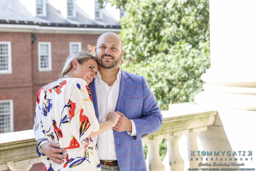 Couple posing on a balcony; the woman leans on the man's shoulder. Both are dressed in formal attire.